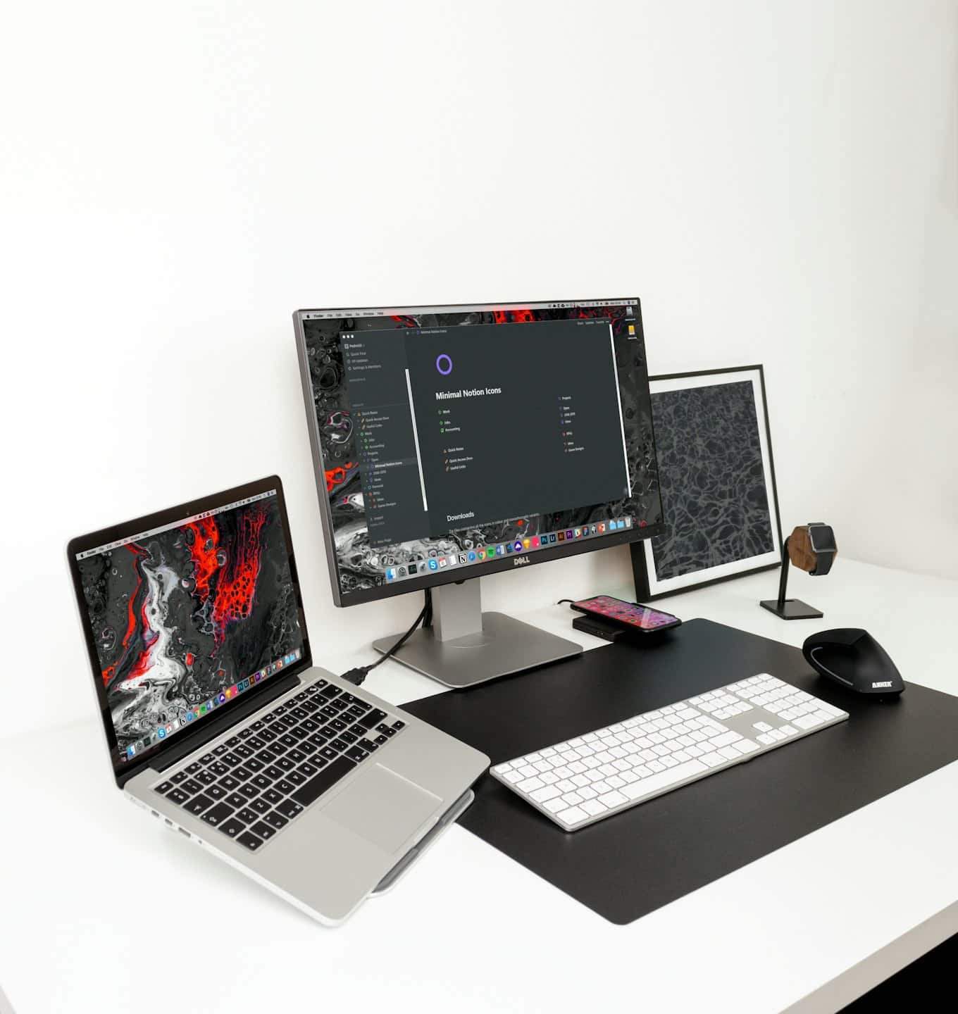 Minimalistický pracovný priestor s notebookom, monitorom a doplnkami na bielom stole.